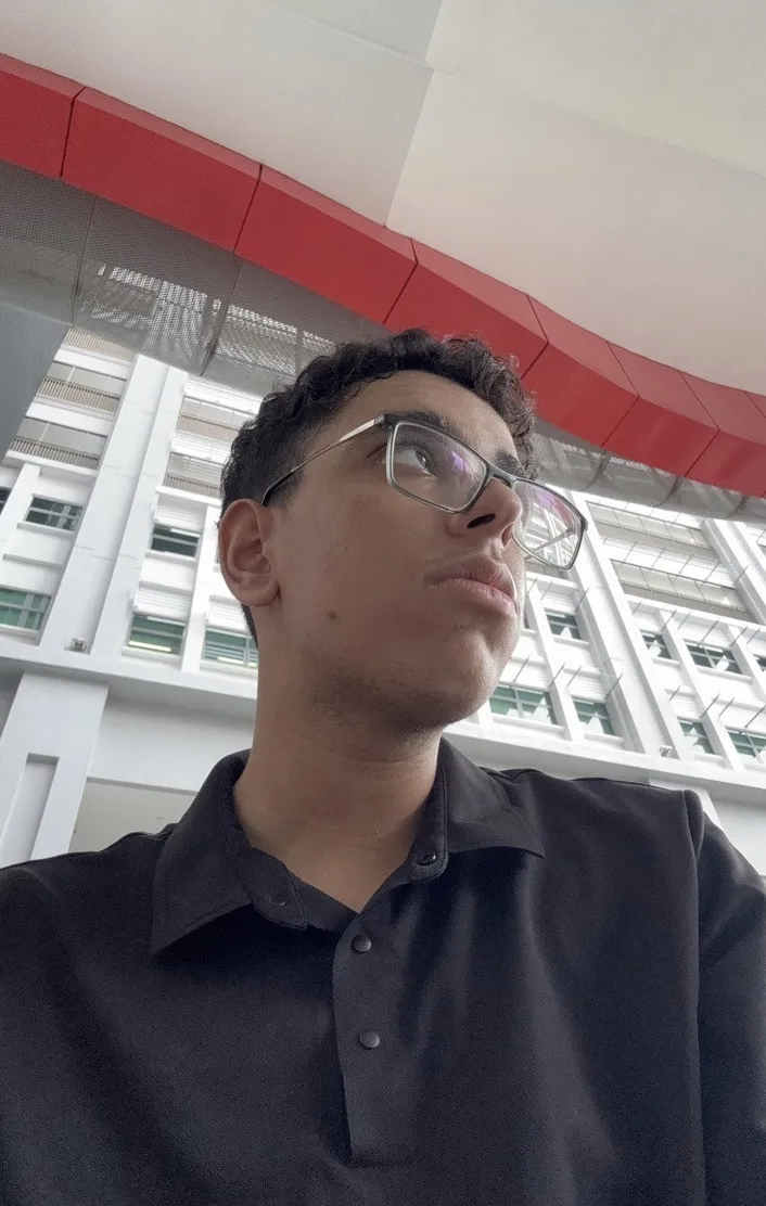 Yousof Selim wearing glasses and a black polo, looking out across a bright atrium.